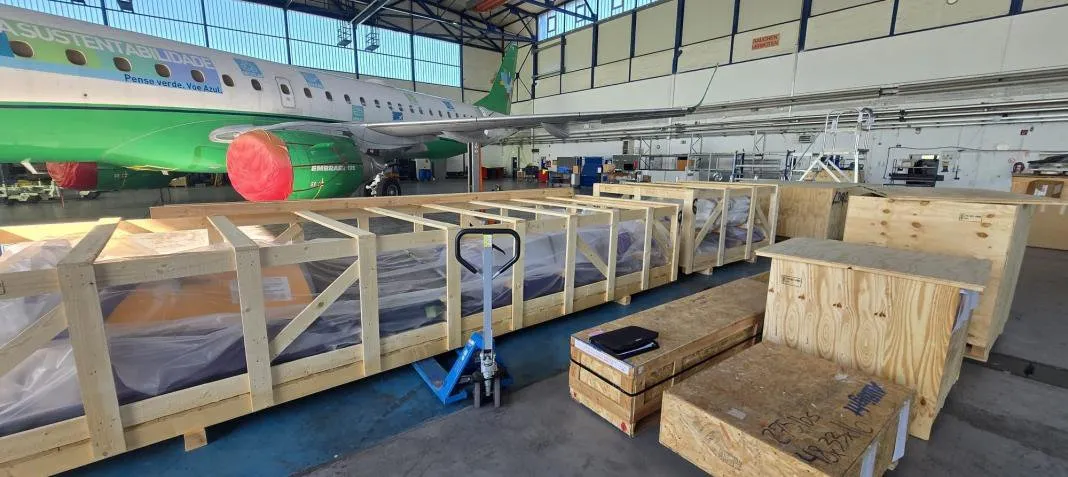 Luftfrachtverschläge mit verpackten Bauteilen in einem Flugzeughangar vor einem Passagierflugzeug